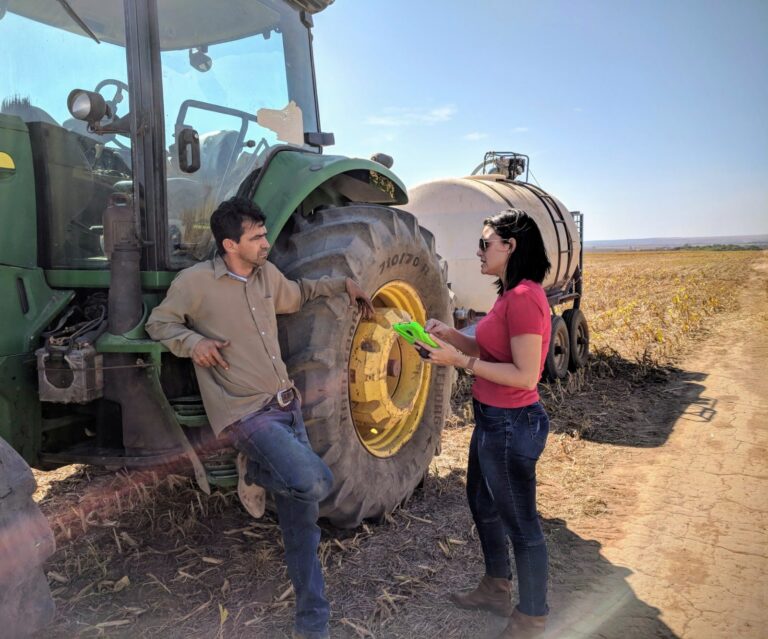 Dr. Ludmila Rattis speaks with a farmer leaning on a tractor.