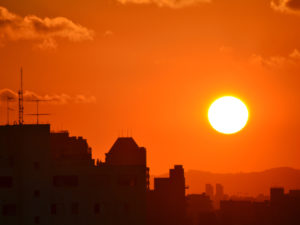 Image of setting sun in a hot-looking orange sky over a city.