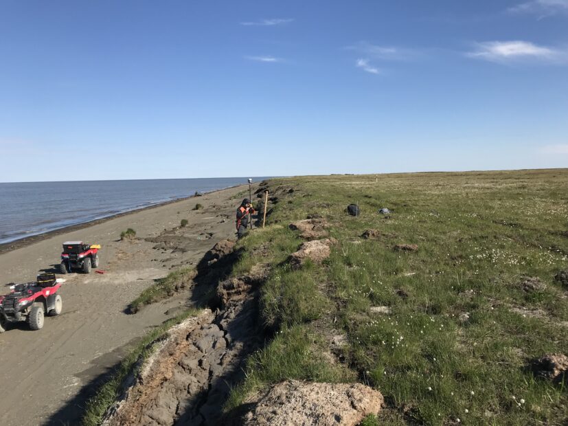 A researcher takes a measurement on a shoreline eroding due to permafrost thaw