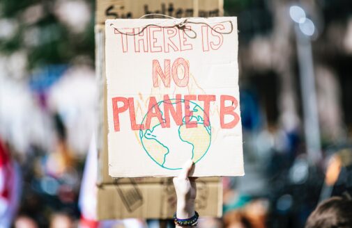 A hand holds a hand-drawn sign that reads "There is no planet B"