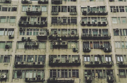 Looking up at a beige apartment complex with many air conditioning units in New Delhi