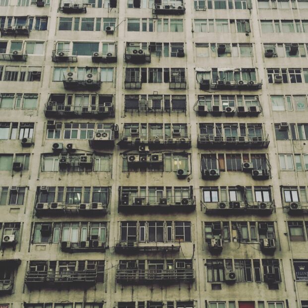 Looking up at a beige apartment complex with many air conditioning units in New Delhi