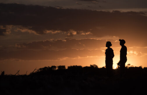 Two human figures darkly silhouetted against an orange sunset