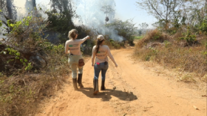 Two researchers walk near burning vegetation in the Amazon