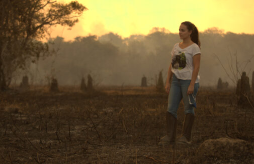 Manoela Machado stands among burned vegetation in a smoky sunset