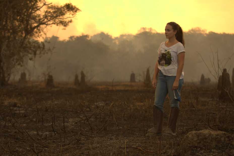 Manoela Machado stands among burned vegetation in a smoky sunset