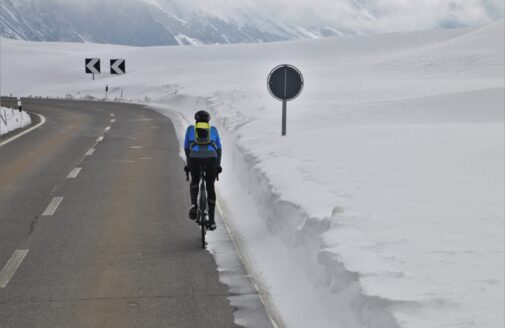 A cyclist rides on a plowed road with snow on either side