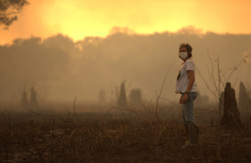 A researcher wearing a mask stands in a smoky, orange-lit landscape