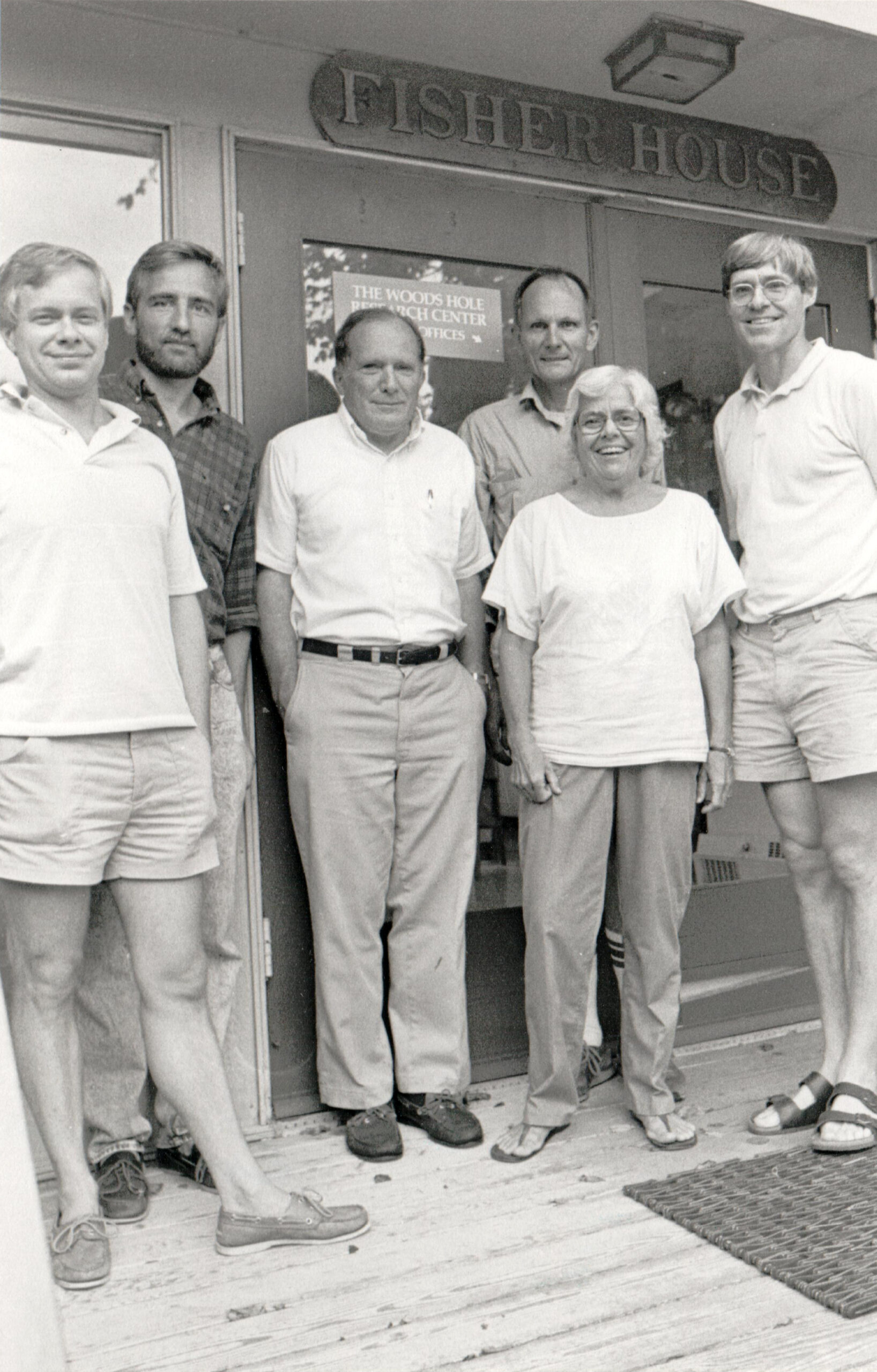 Tom Stone, Foster Brown, George Woodwell, Walter Matherly, Katharine Woodwell, Skee (Richard) Houghton stand in front of Fisher House in an old black and white photograph.