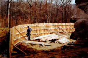 A worker stands next to a wooden wall, under construction to become the new wing of the Woodwell Climate main building.