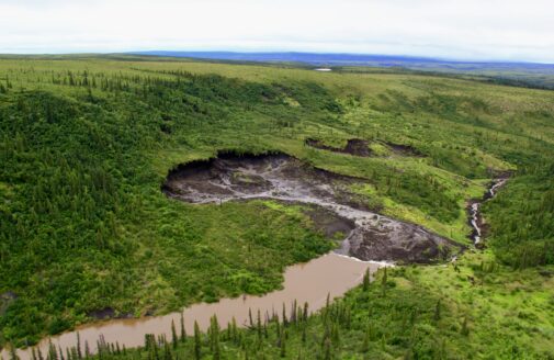 A river drops off where it intersects with a large thaw slump, which has eroded tons of soil from the landscape