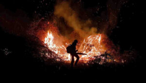 A firefighter is silhouetted against a nighttime blaze