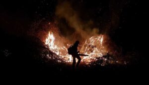 A firefighter is silhouetted against a nighttime blaze