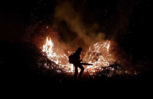 A firefighter is silhouetted against a nighttime blaze