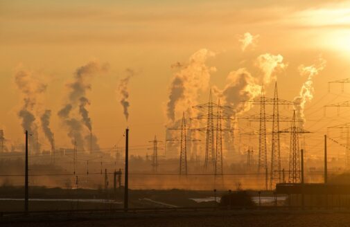 Smokestacks release plumes of exhaust into an orange sky