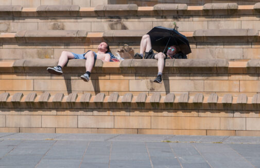 two men reclining on steps under umbrella in attempt to cool off