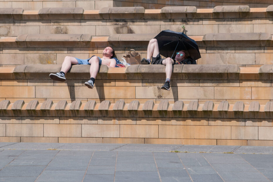 two men reclining on steps under umbrella in attempt to cool off