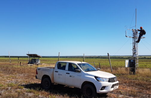 a truck stands in the foreground while a person works at the top of a tower 3-4 times their height to adjust scientific instruments