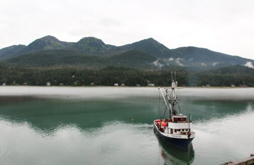 A fishing vessel floats on the water in the foreground, with mountains in the background