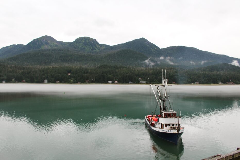 A fishing vessel floats on the water in the foreground, with mountains in the background