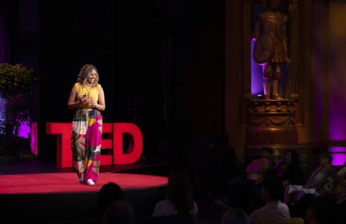 ludmila rattis standing in front of a TED sign on stage giving a ted talk