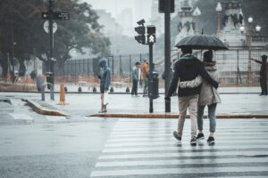 a couple walks on a crosswalk in the rain under an umbrella