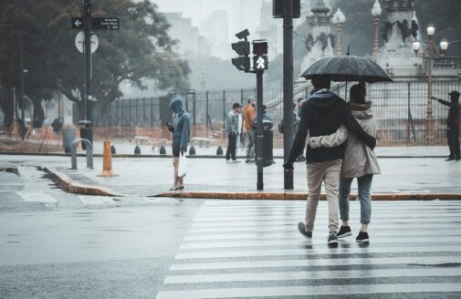 a couple walks on a crosswalk in the rain under an umbrella