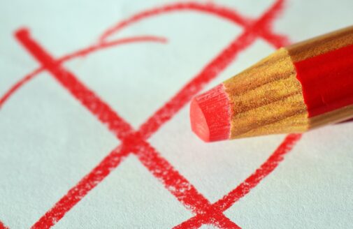 a red colored pencil in the foreground, a red x in a circle drawn in the background