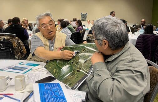 Two older men hold a laminated map, pointing to something on the map