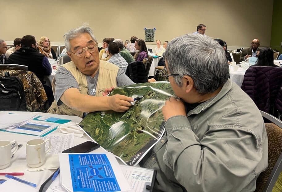 Two older men hold a laminated map, pointing to something on the map