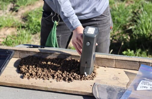 colleen smith scans a tray of crumbled soil with a grey soil spectrometer