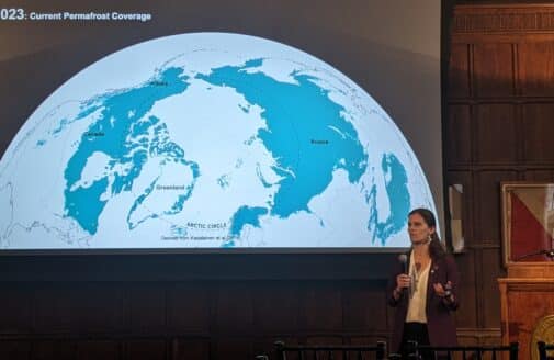 a woman speaks into a microphone in front of a large projected map of the northern hemisphere, showing permafrost extent