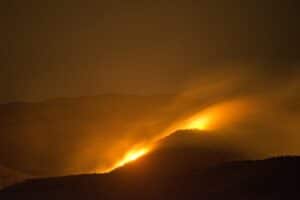 A wildfire at night on a mountain, giving off a fuzzy orange glow