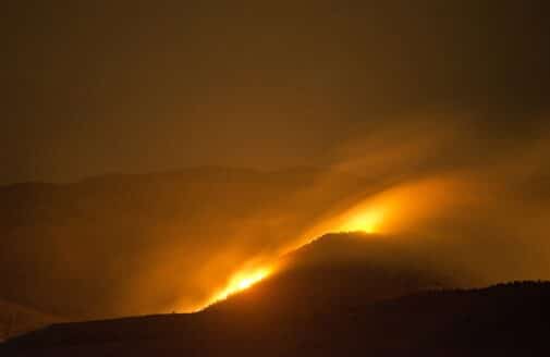 A wildfire at night on a mountain, giving off a fuzzy orange glow