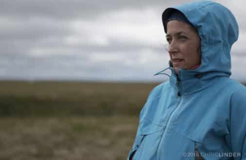 Sue Natali looks to the left, wearing a blue jacket in an open landscape