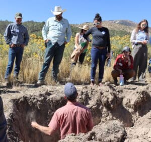 a group of people look at a man standing in a deep hole in the dirt