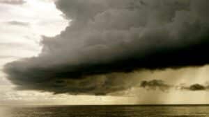 a dark stormcloud dumps rain over an open body of water