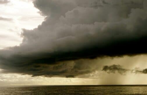 a dark stormcloud dumps rain over an open body of water