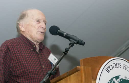 George Woodwell stands at a podium speaking at an event under a tent