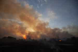 smoke rises into a dim sky as the sun sets over the Pantanal