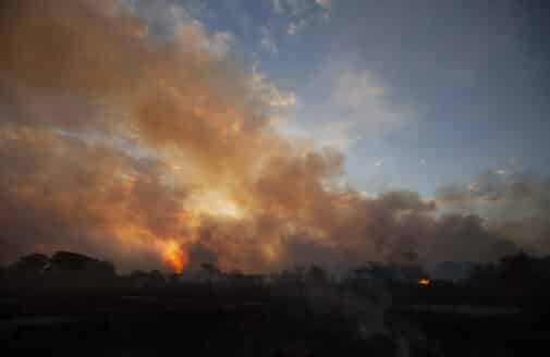 smoke rises into a dim sky as the sun sets over the Pantanal