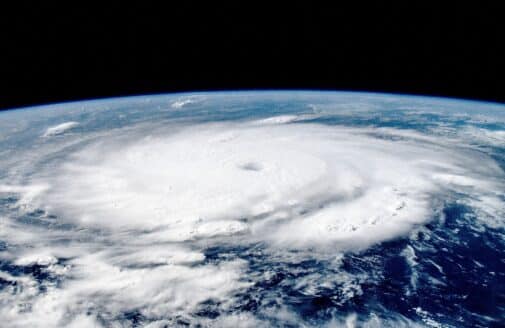 a satellite image shows the large, swirling white clouds of Hurricane Beryl in the atmosphere, with the curve of the earth visible