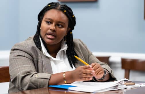 Natalie Baillargeon sits at a desk, speaking to someone out of frame while holding a pencil