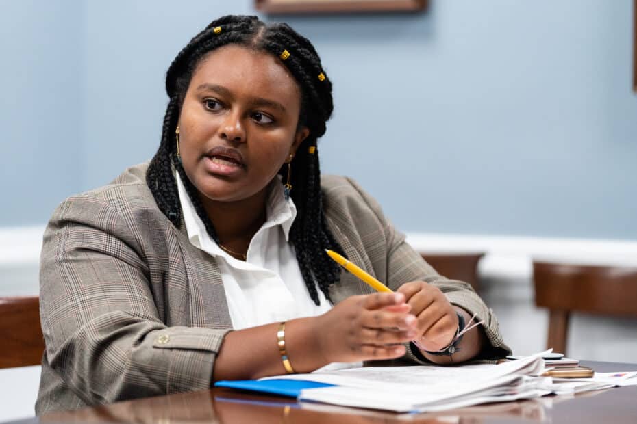 Natalie Baillargeon sits at a desk, speaking to someone out of frame while holding a pencil