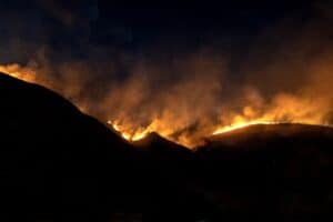 a nighttime photograph of an orange brush fire illuminating the dark outline of hills