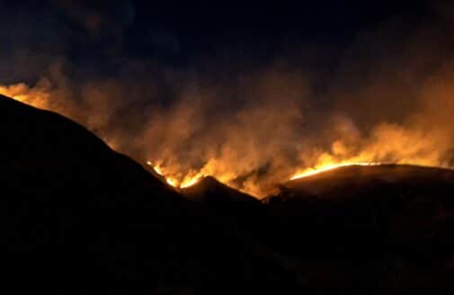 a nighttime photograph of an orange brush fire illuminating the dark outline of hills