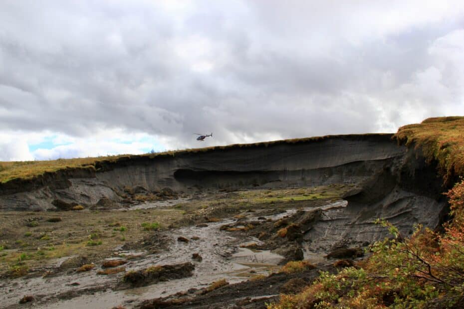 thaw slump in arctic tundra with helicopter flying overhead